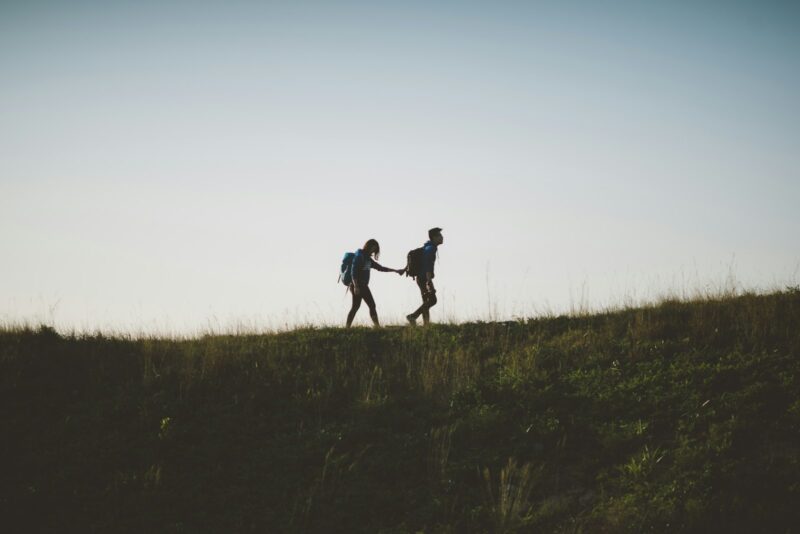 couple walking on hill while holding during daytime signifying trust