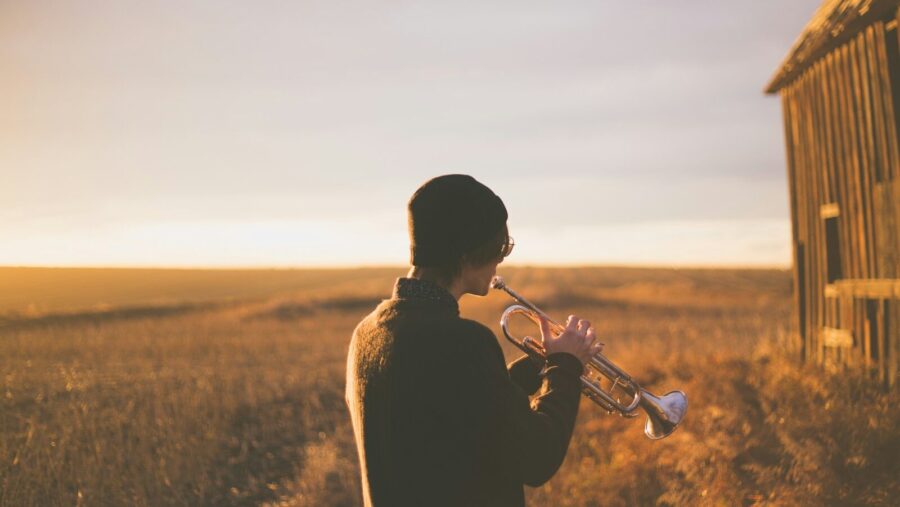 man playing trumpet outside house on field during daytime, listening skills