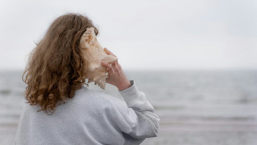 a woman holding a seashell up to her face, listening skills