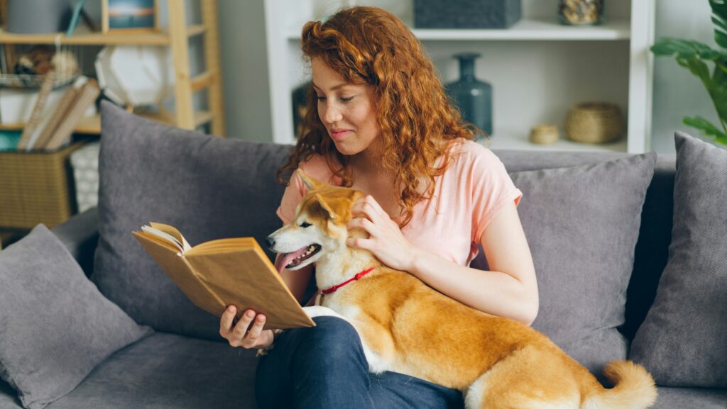 a woman sitting on a couch with a dog reading a book