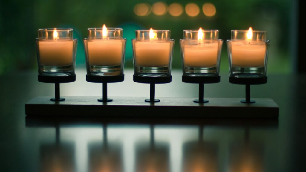 bokeh photography of five lighted votive cadles